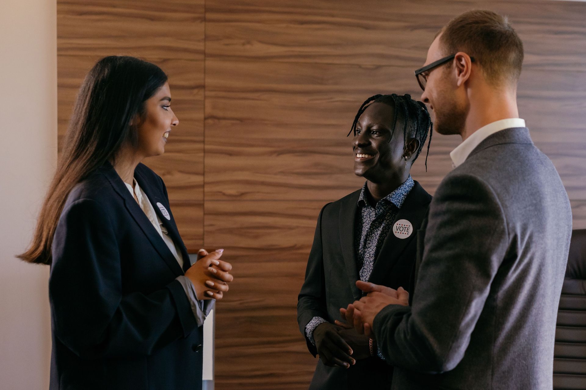 Three people in business attire talking in a wood-paneled office setting