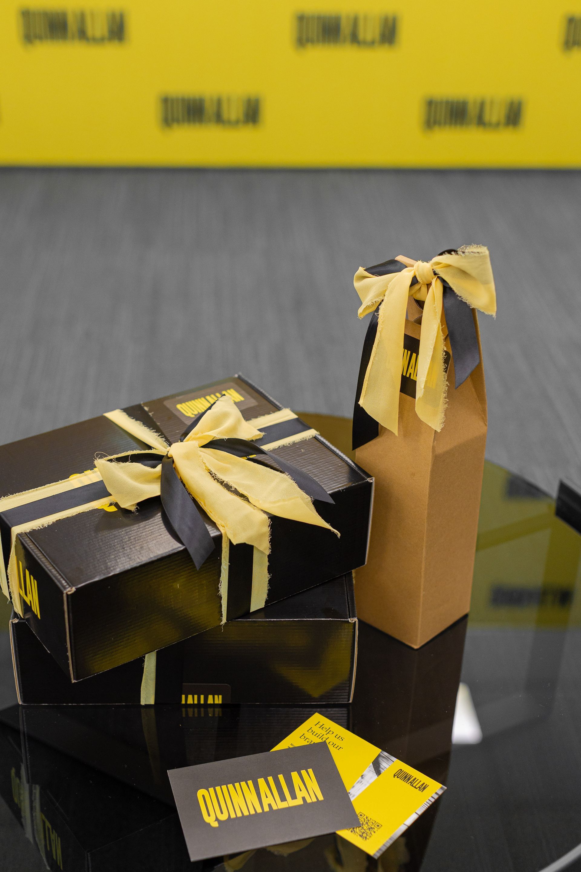 Black and gold gift boxes tied with ribbon on a reflective table against a yellow backdrop