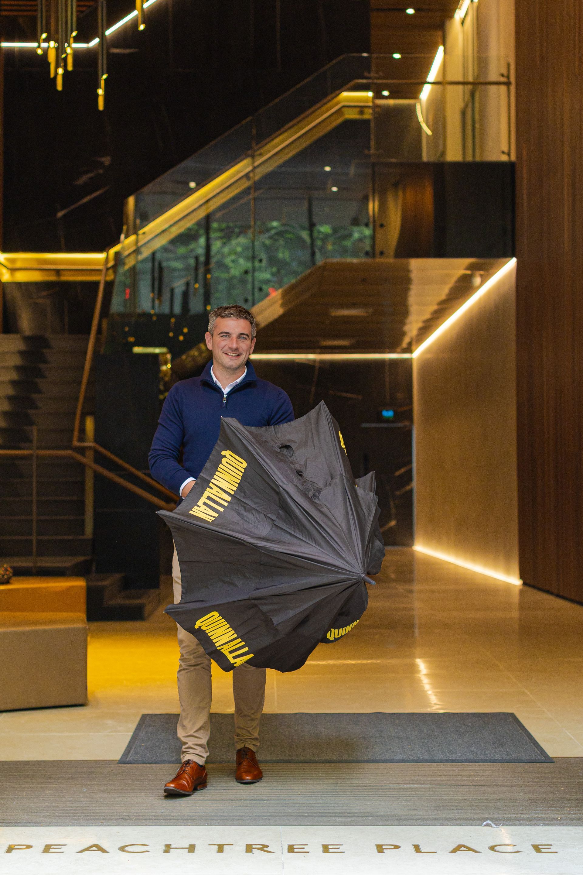 Person in a blue shirt holding an open black umbrella in a modern lobby.