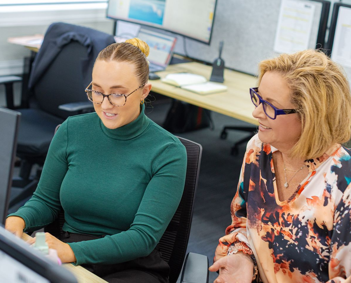 Two coworkers working at computers in an office, smiling and focused on the screen.