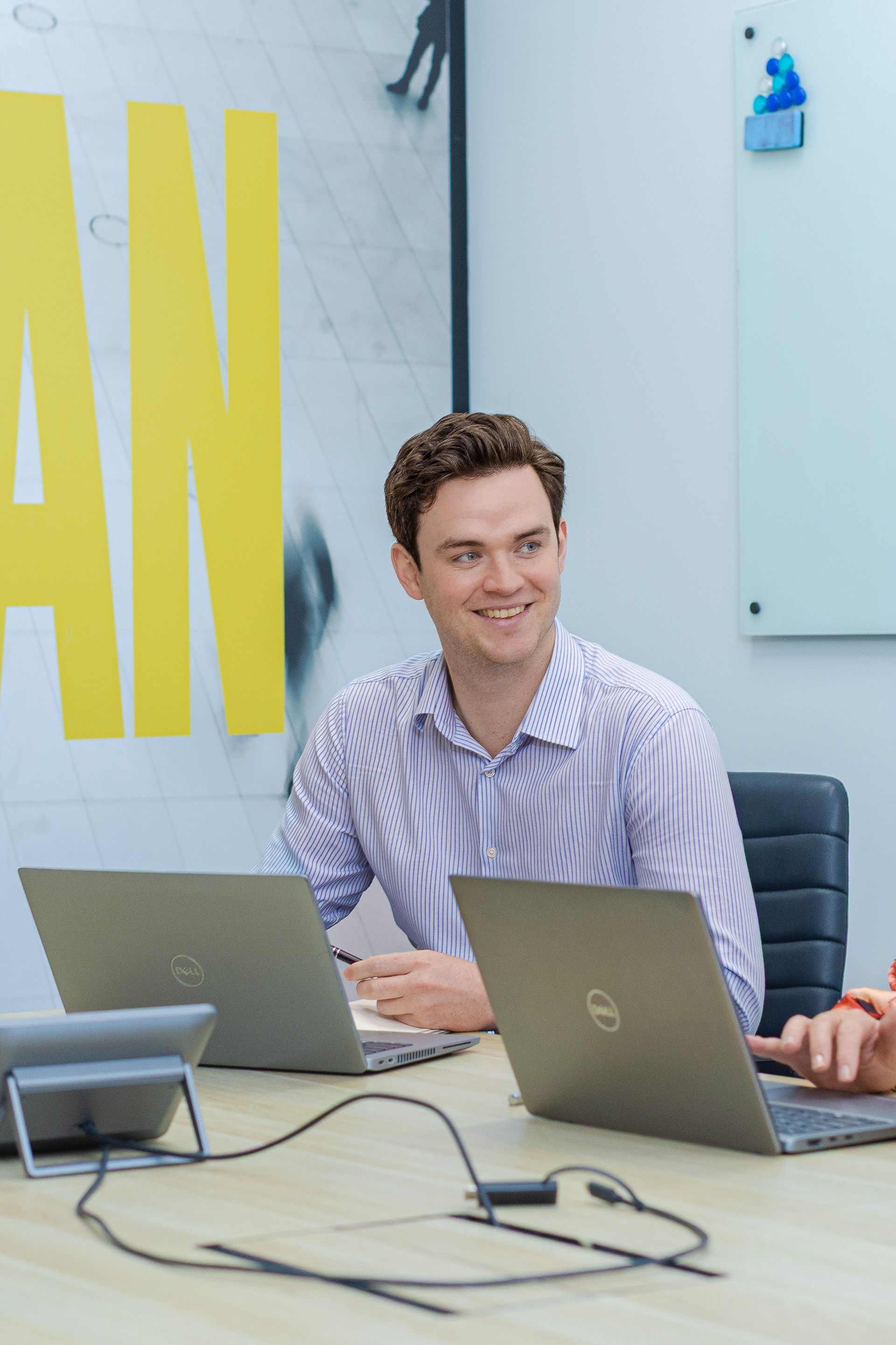 Man smiling at a conference table with laptops in a bright meeting room