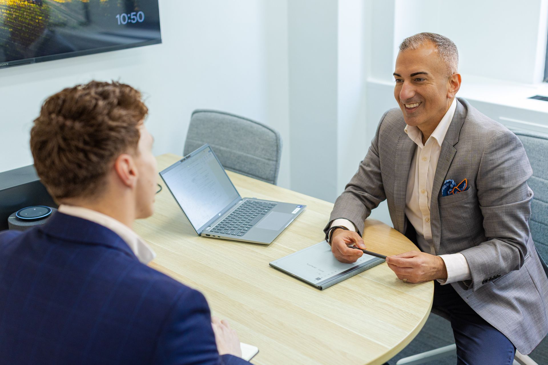 Two people meeting at a table in a bright office, with a laptop and papers between them.