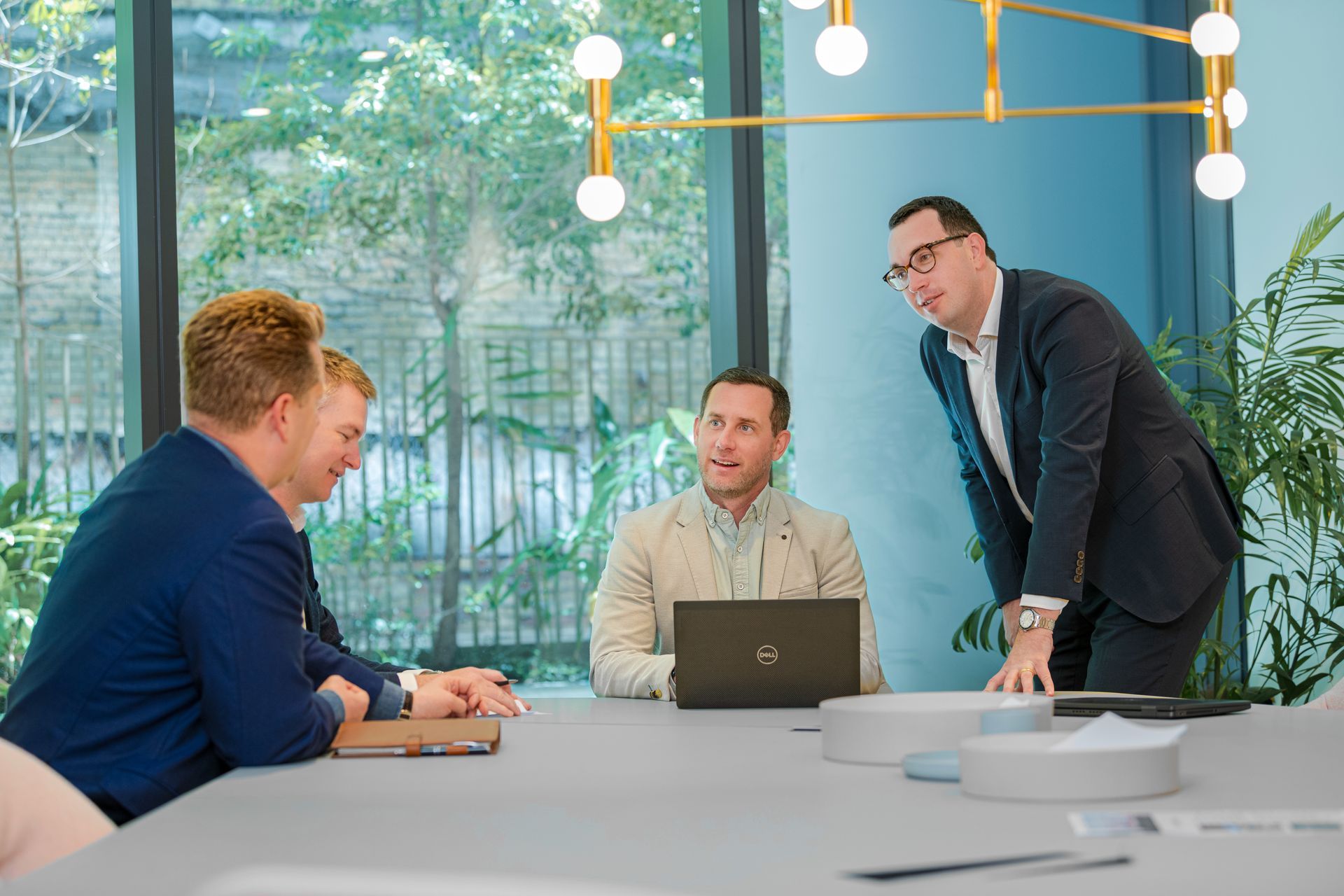 Three coworkers reviewing documents together in a bright office, standing in front of a textured wall.