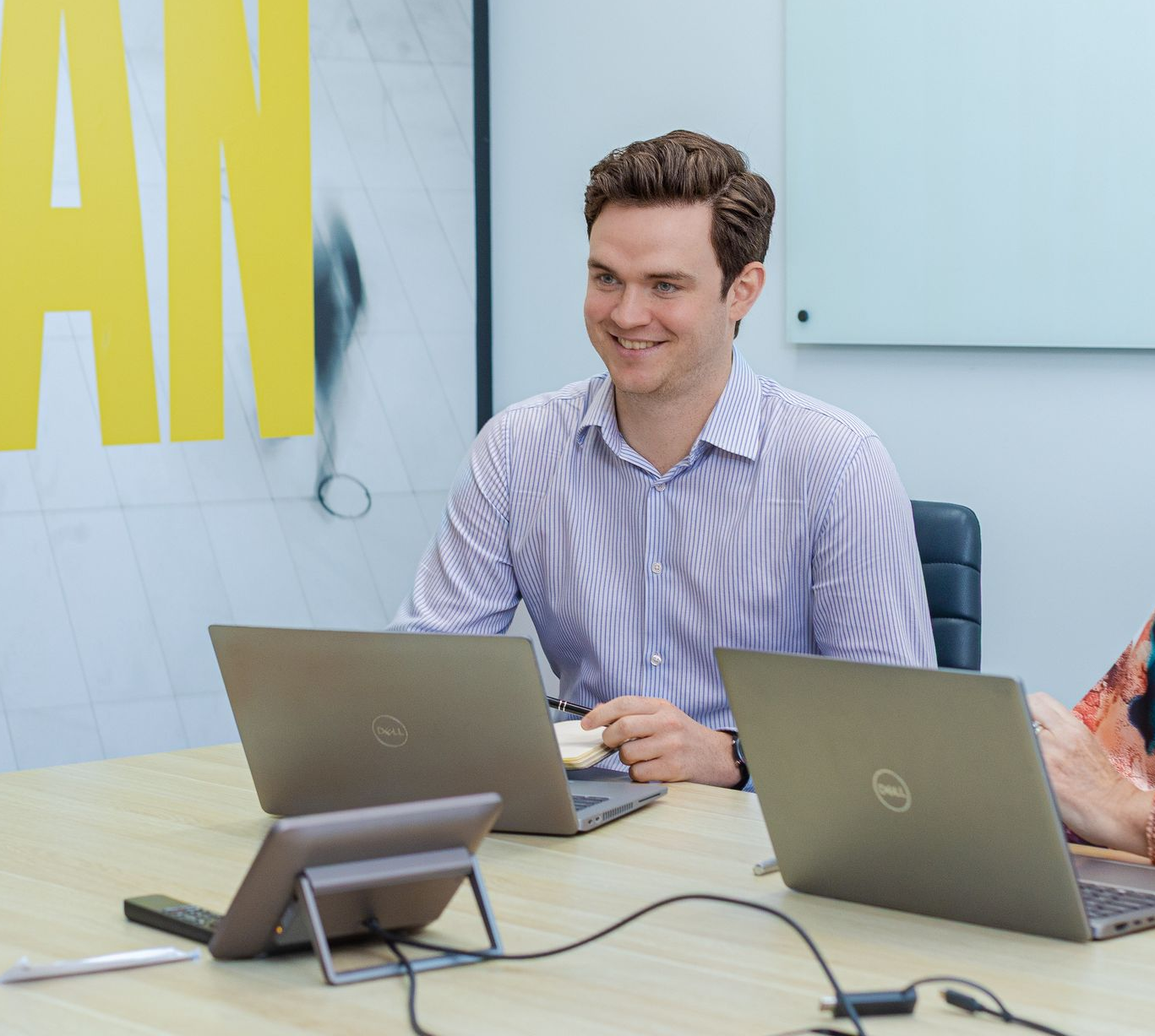 Two people in a meeting room, smiling behind open laptops at a conference table.