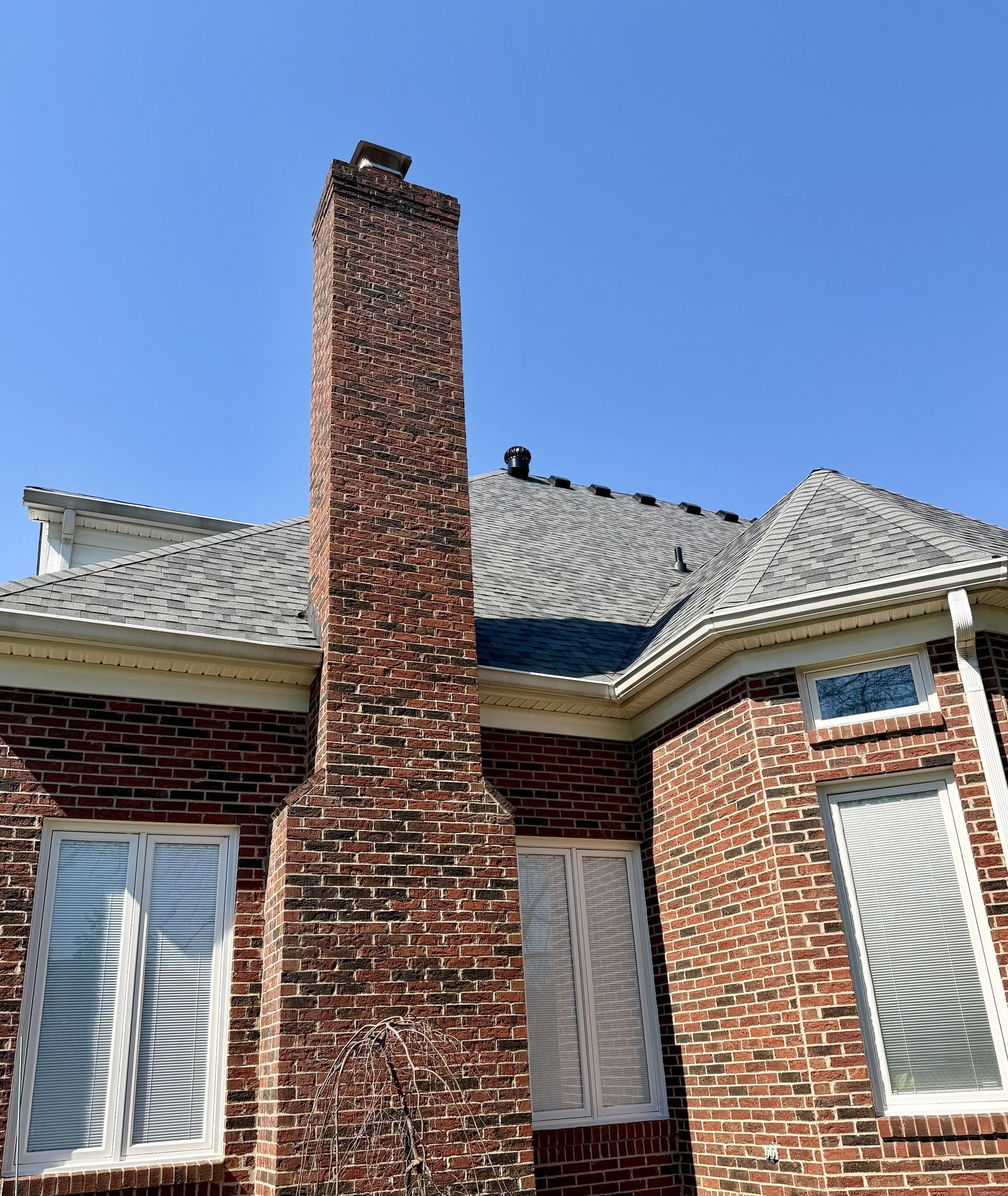 Brick chimney with chimney cap on a home with a new shingle roof