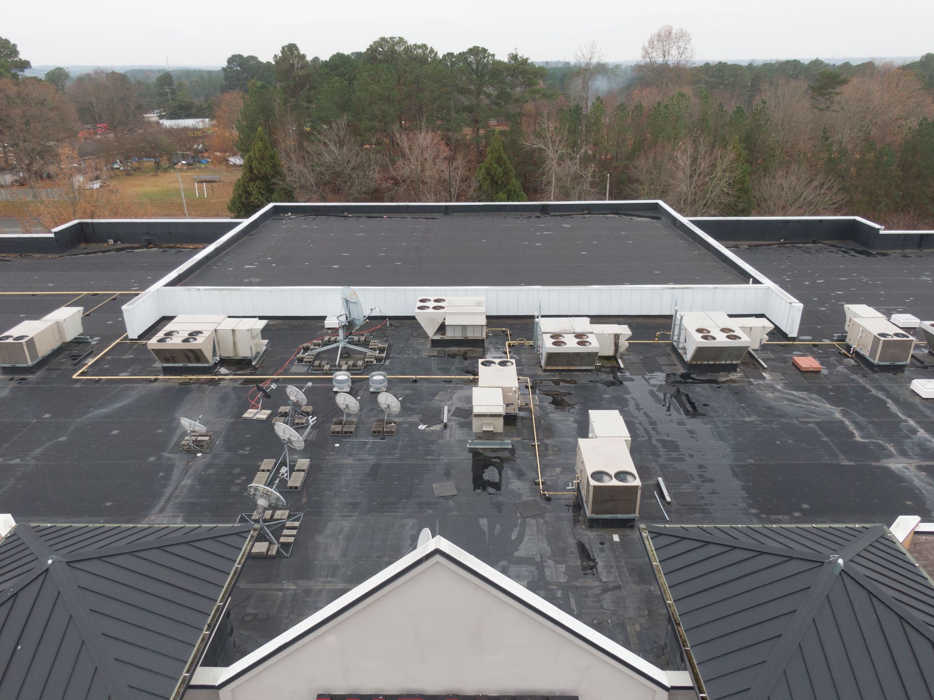 Aerial view of a flat commercial roof with multiple HVAC units, drainage patches, and a pitched roof section in the front.
