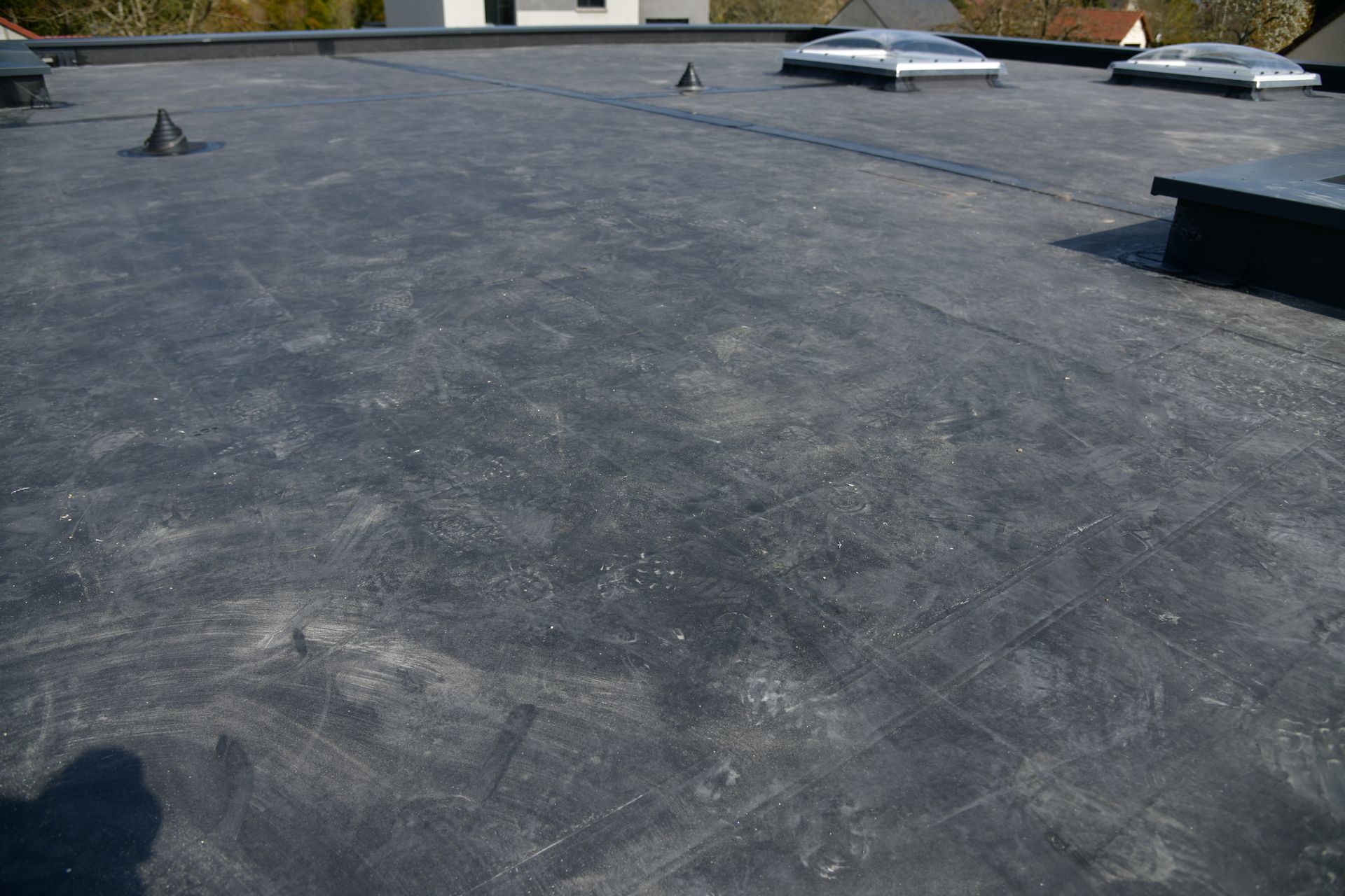 A flat, dark gray roof surface with several small vents and two skylights under a bright, sunny sky.
