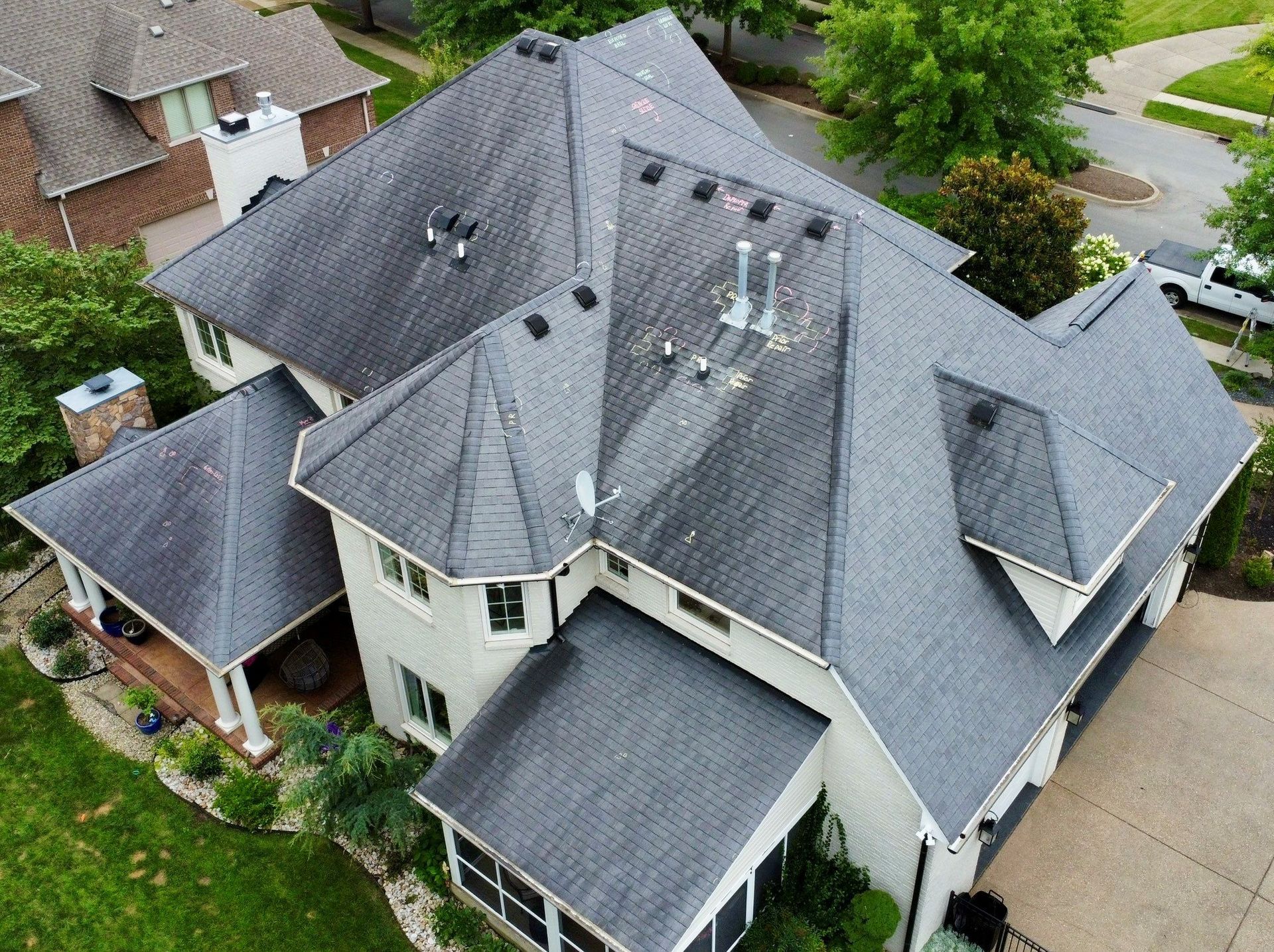 Aerial view of a large residential home with a multi-gabled dark shingle roof, white siding, and surrounding green lawn.