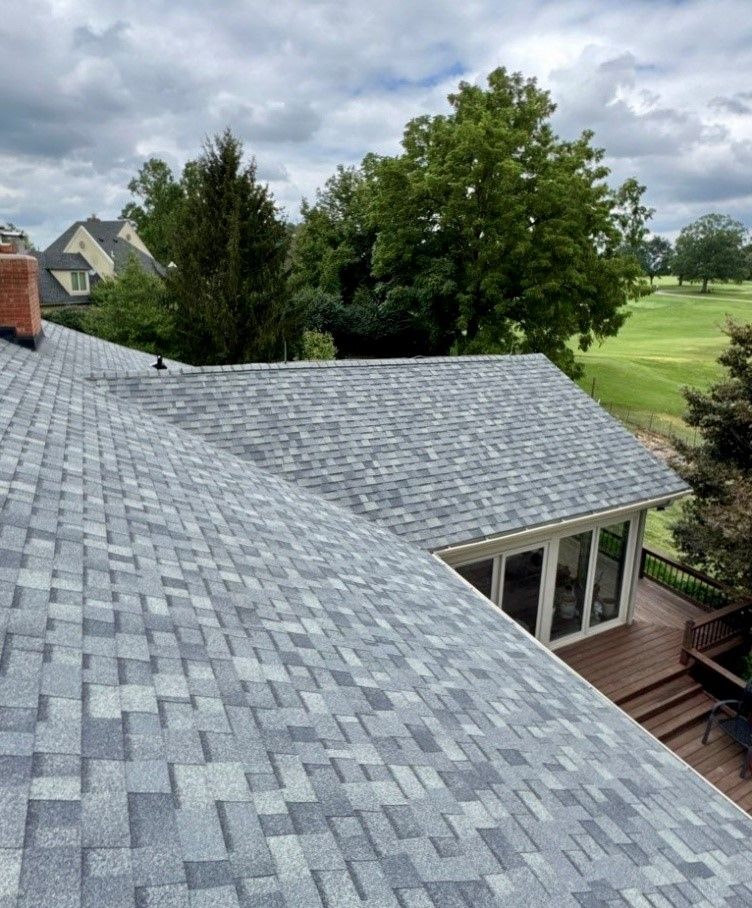 A high-angle view of a gray shingled roof with a wooden deck and green golf course in the background.