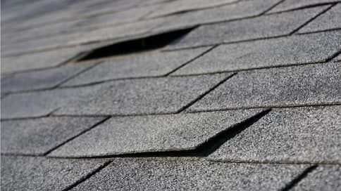 A section of a gray shingled roof showing curled edges and a missing shingle, indicating wear and potential damage.