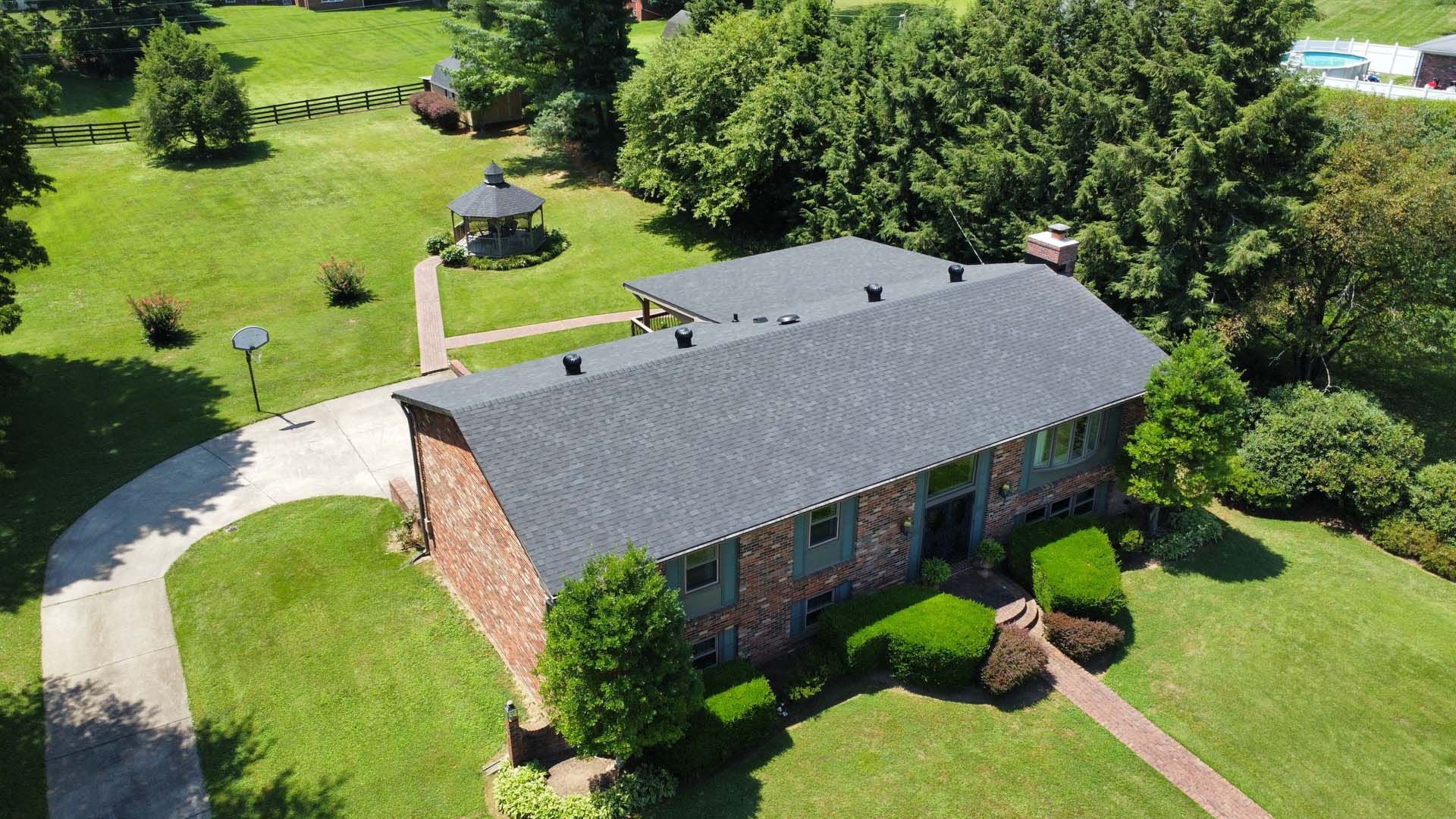 Aerial view of a two-story brick house with a dark shingled roof, a front walkway, a gazebo, and a large grassy yard.