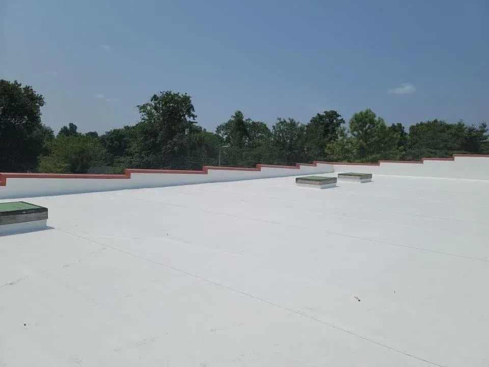 A bright, flat white rooftop with several rectangular skylights, bordered by a low wall with a red-orange trim.