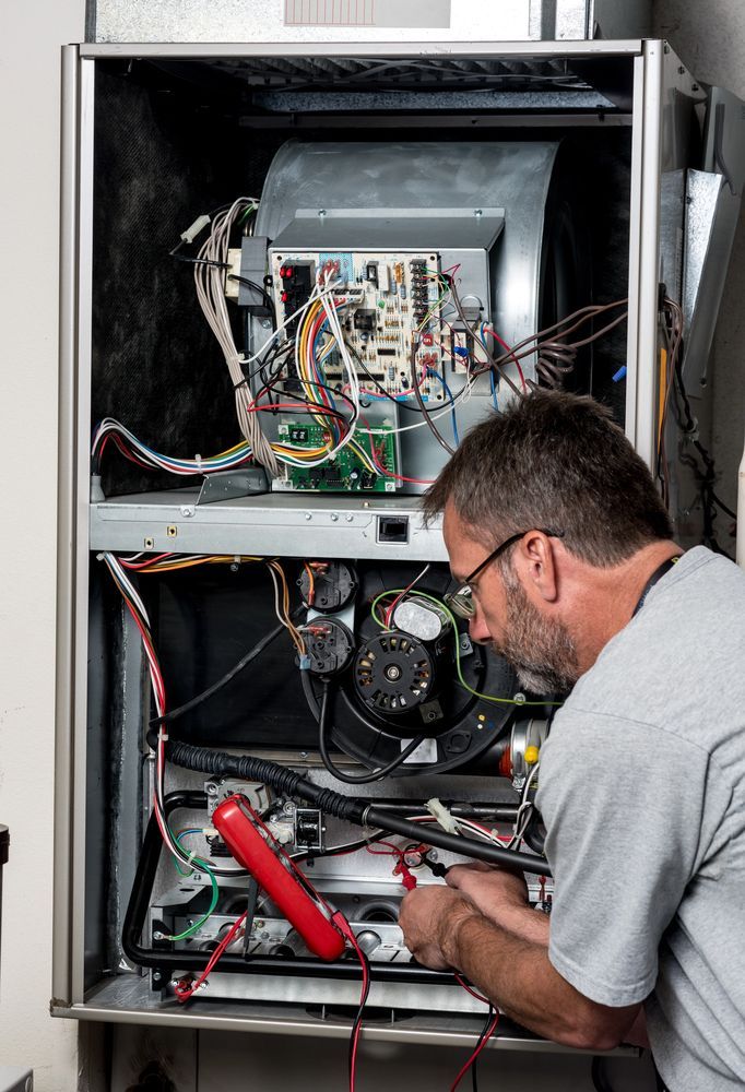 HVAC technician repairs furnace, using multimeter. Inside a metal unit, with wires and electrical components.