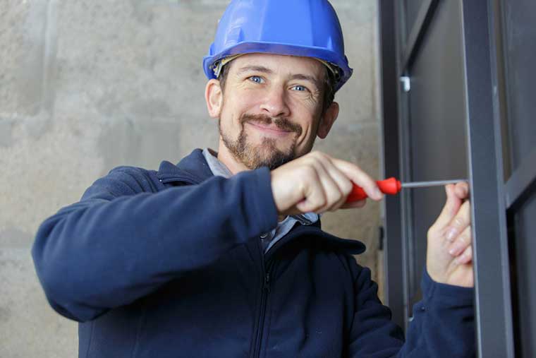 A man wearing a hard hat is using a screwdriver to fix a door.