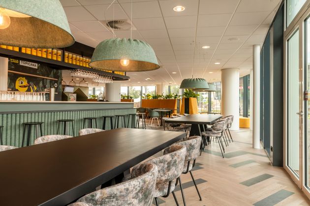 Modern café-interieur met houten tafels, gestoffeerde zitbanken en warme houten accenten aan het plafond.