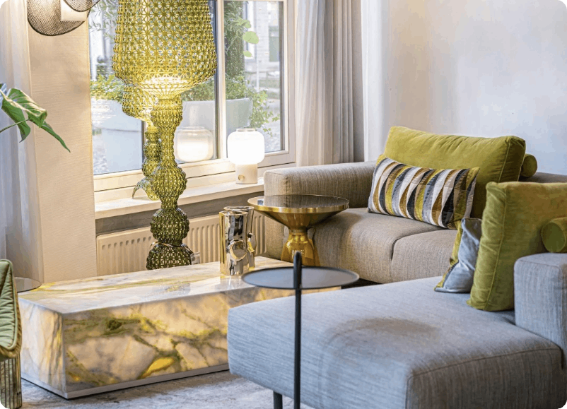 Moderne woonkamer met grijze bank, groene stoel, marmeren tafel en gouden staande lamp bij een licht raam.