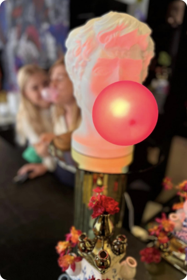 Een gloeiend rode ballonlamp onder een wit pastelkleurig beeldhouwwerk met bloemen op de voorgrond.