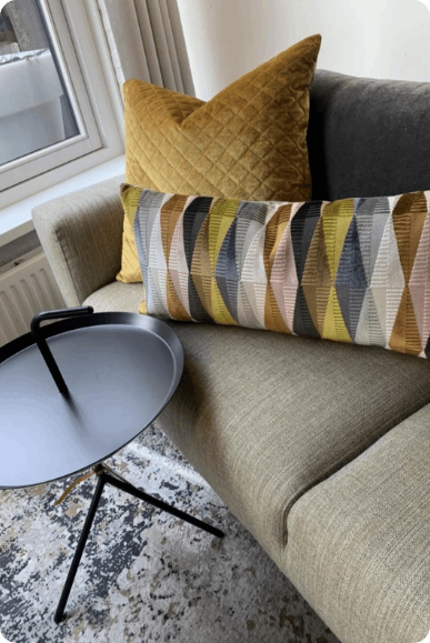 Moderne zithoek in de woonkamer met een beige bank, kussens met patroon en een rond bijzettafeltje bij het raam.