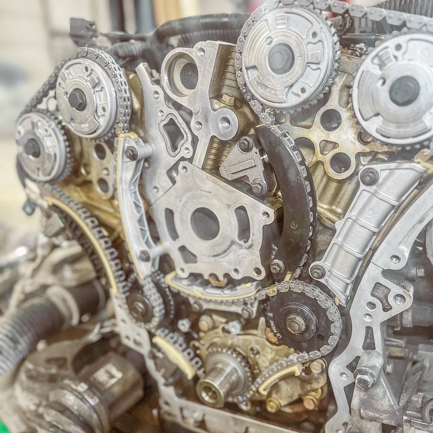 Close-up of a metal engine timing assembly with gears, chains, and sprockets on a workbench | Proving Ground Automotive