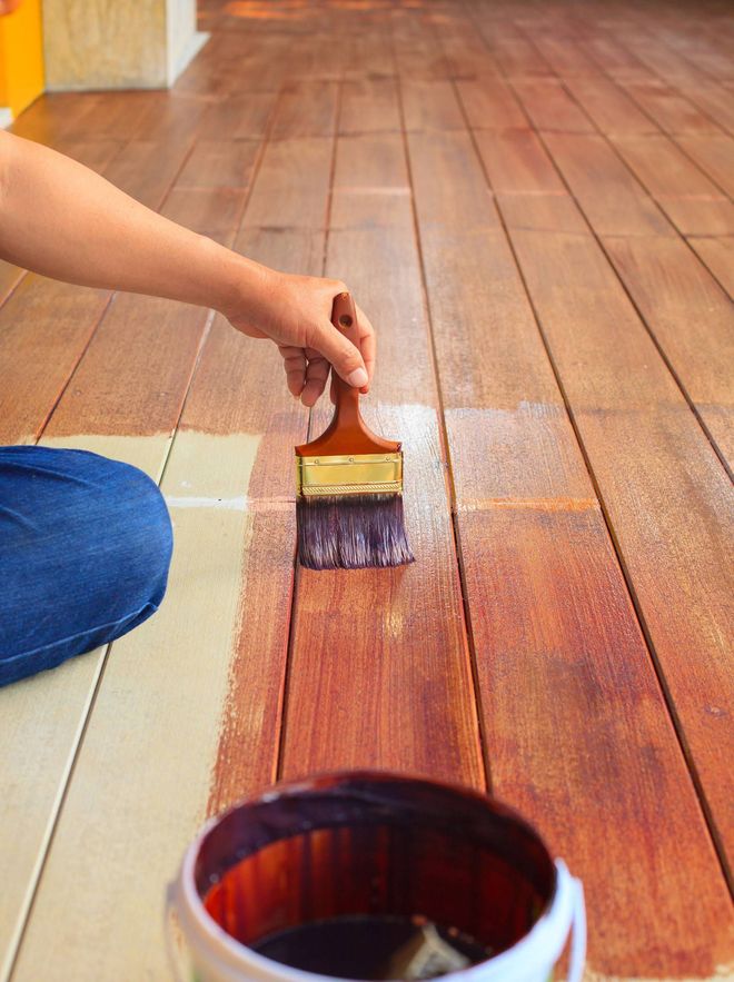 Hand brushing reddish stain onto a wooden floor, with a paint can in the foreground