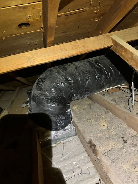 Black insulated HVAC duct runs through an attic under wooden rafters.