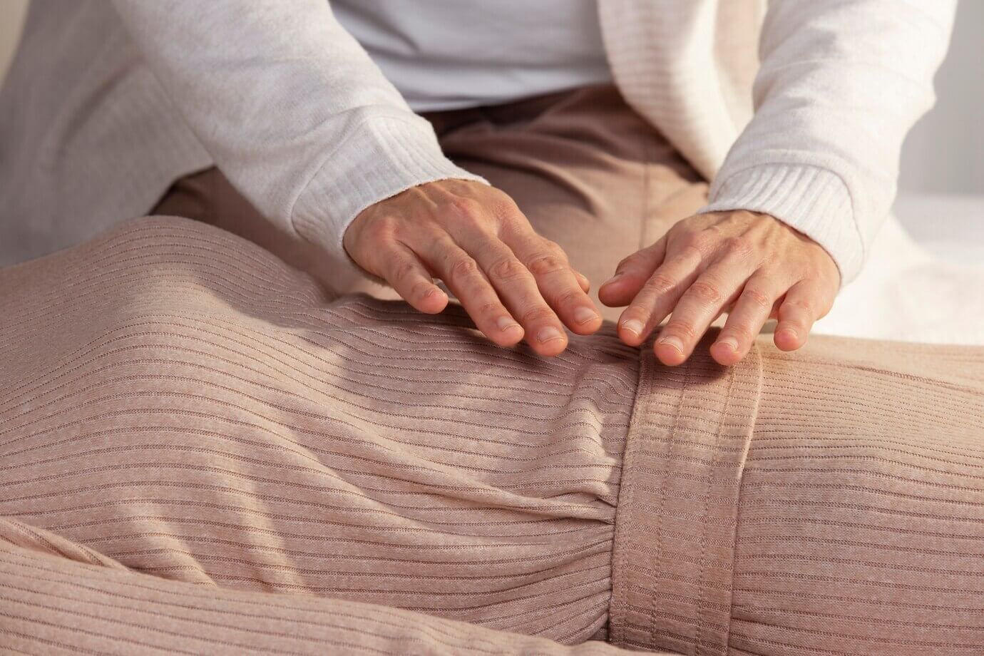 Una mujer está sentada en una cama con las manos en las rodillas.