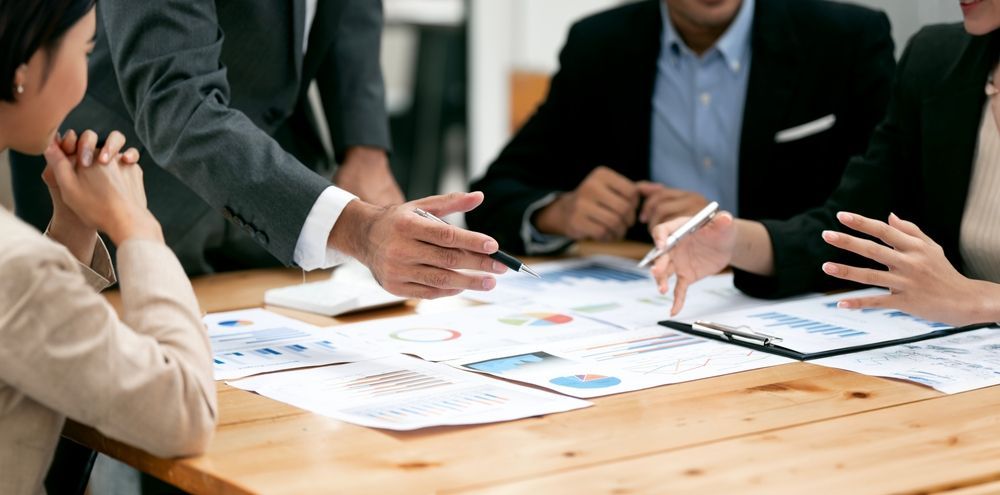 Business professionals collaborating around a wooden table, reviewing financial charts and documents during a meeting.