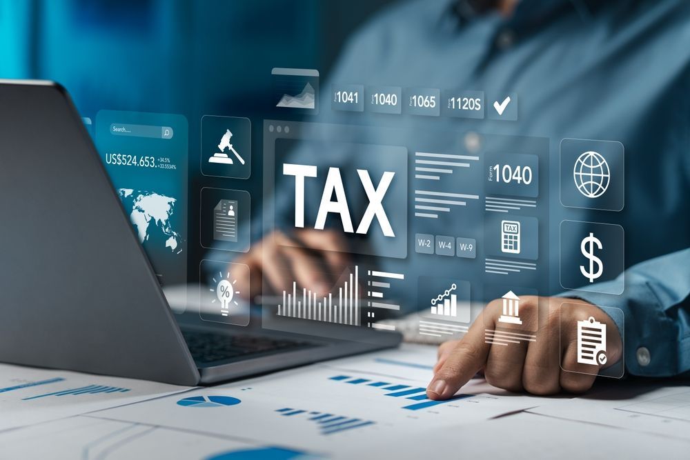 A person works on a laptop with holographic icons of tax documents, financial charts, a globe, and currency symbols.