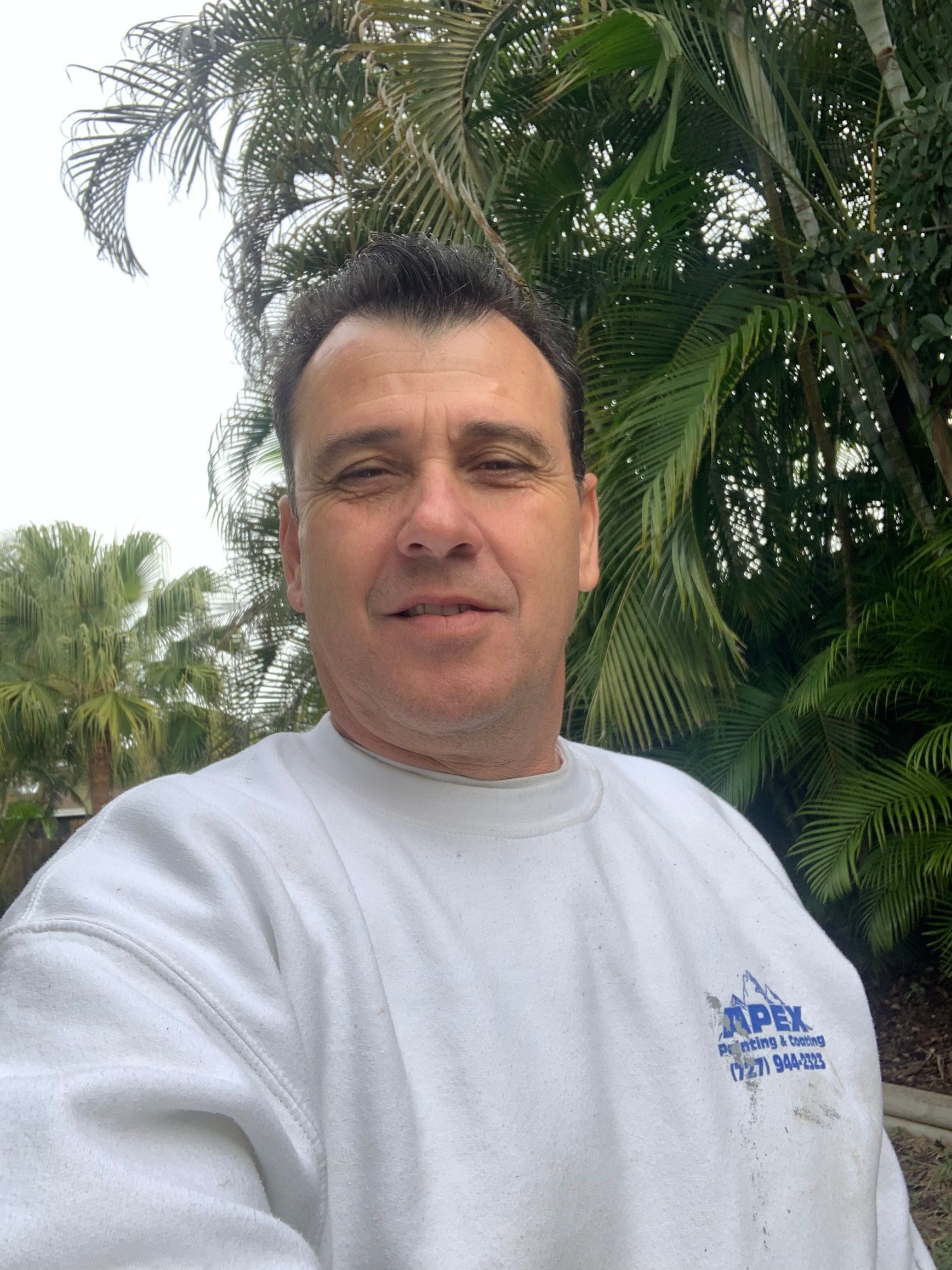 A man is taking a selfie in front of a lush green forest.
