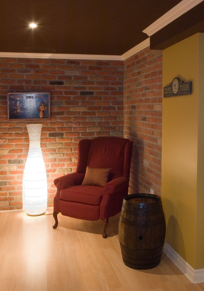 Fauteuil rouge, mur de briques, vase lumineux, tonneau en bois et mur doré dans une pièce chaleureuse.