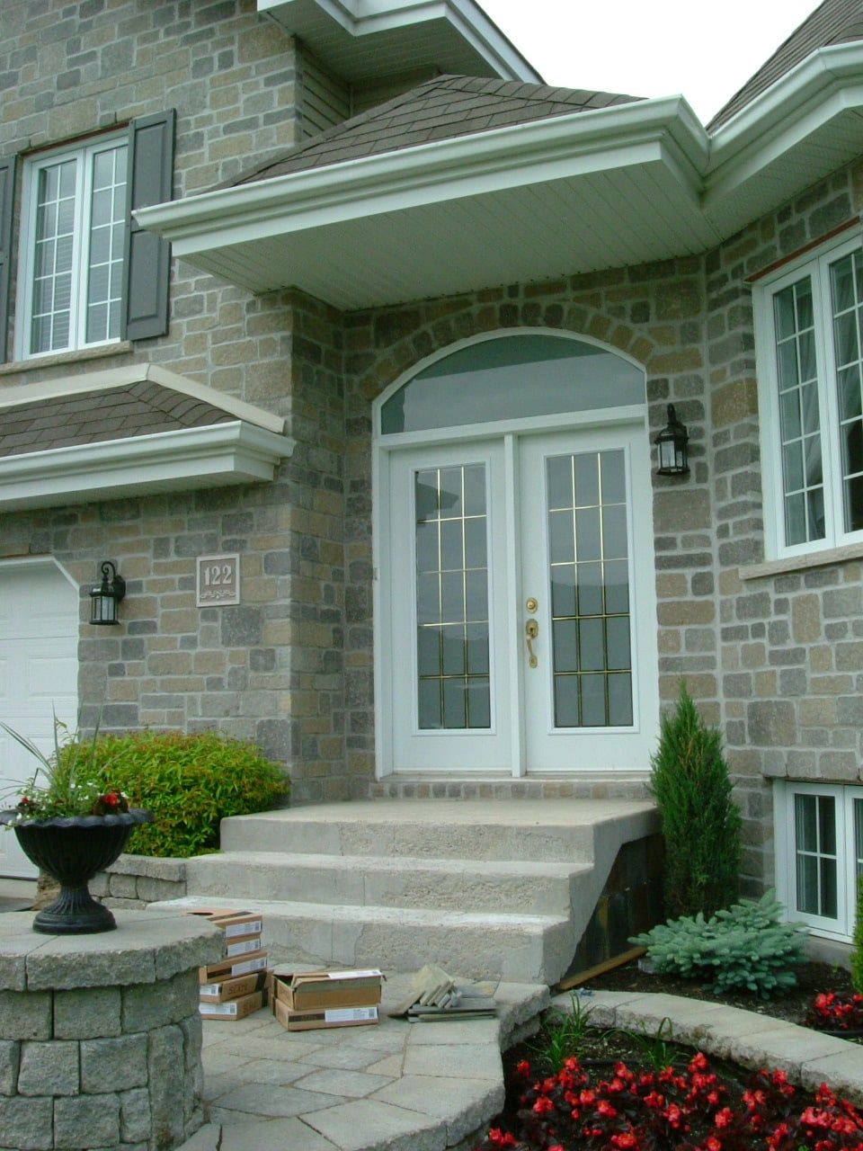 Entrée de maison en pierre avec double porte, marches et aménagement paysager.