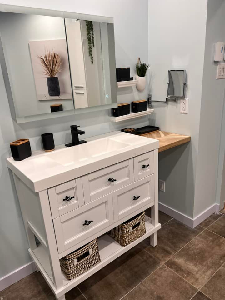 Meuble-lavabo blanc avec poignées noires, miroir et étagères, à côté d'un petit comptoir en bois.