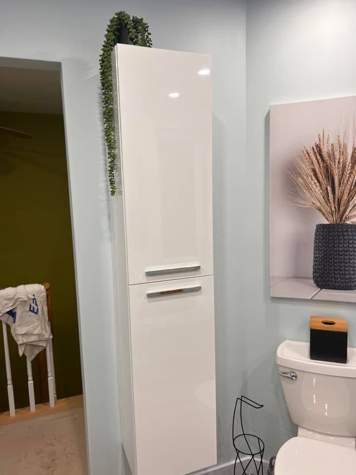 Meuble de salle de bain blanc haut avec plante suspendue et toilettes à côté.