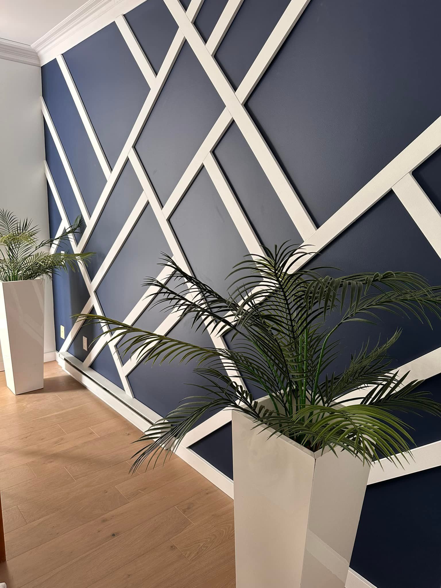 Mur bleu avec des ornements géométriques blancs, deux jardinières blanches avec des plantes vertes, parquet clair.
