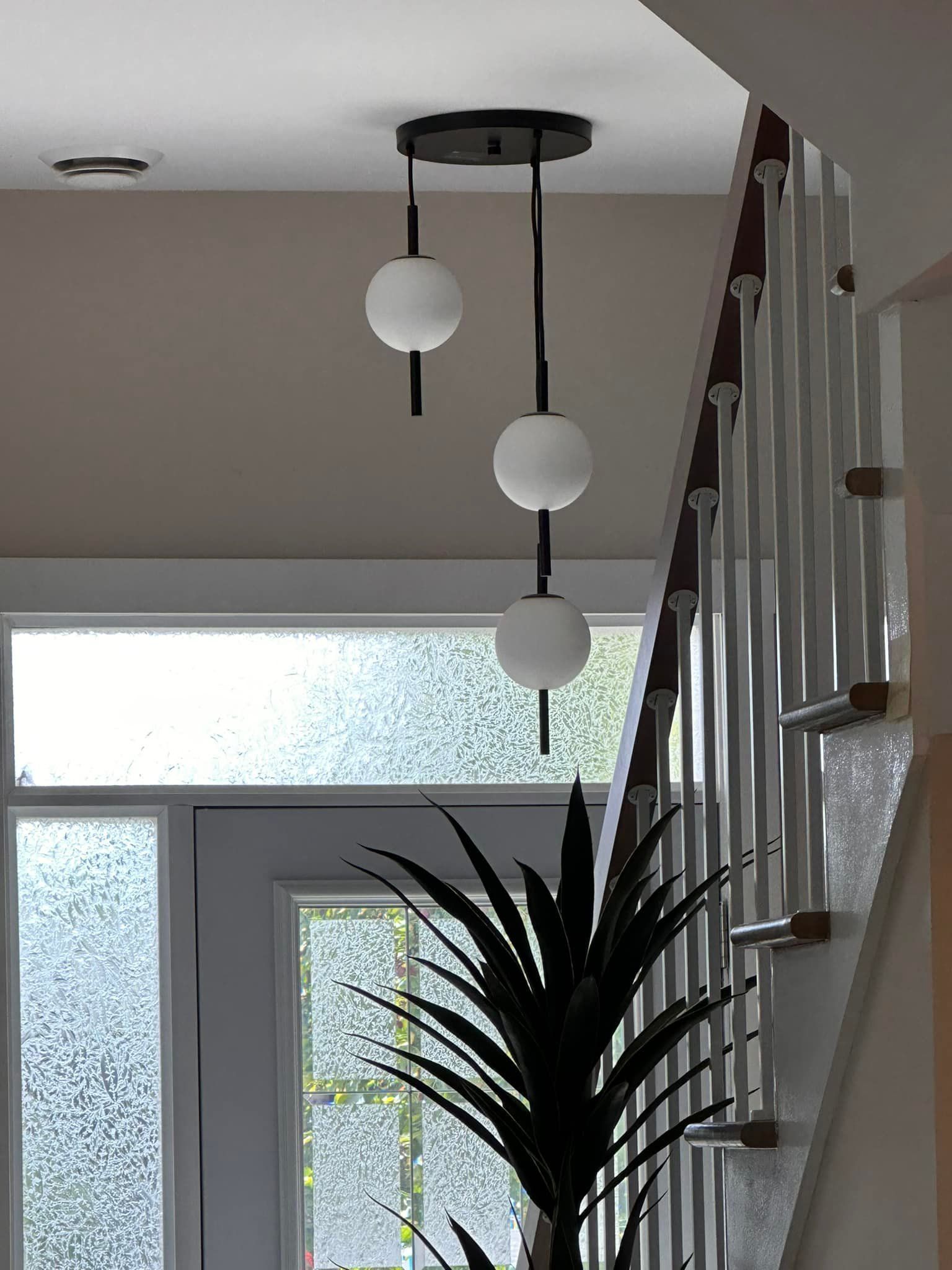 Un luminaire suspendu en forme de globe noir et blanc est installé près d'un escalier et d'une porte en verre dépoli.