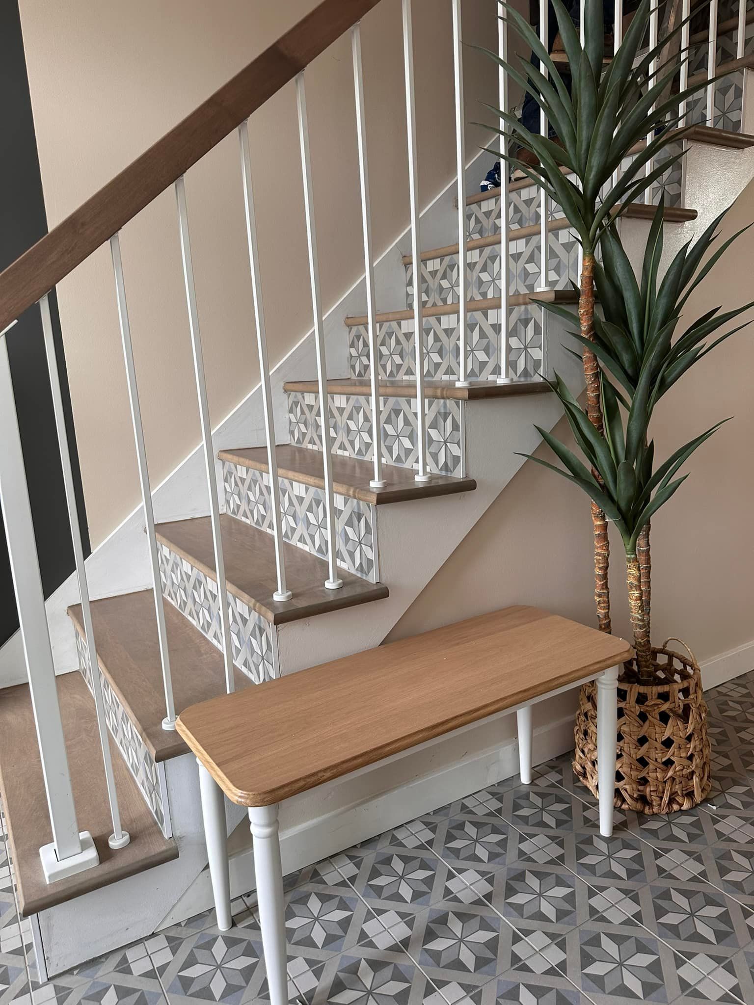 Escalier avec contremarches à motifs, rampe en bois, balustres blancs et banc en bois. Grande plante en pot à côté de l'escalier.