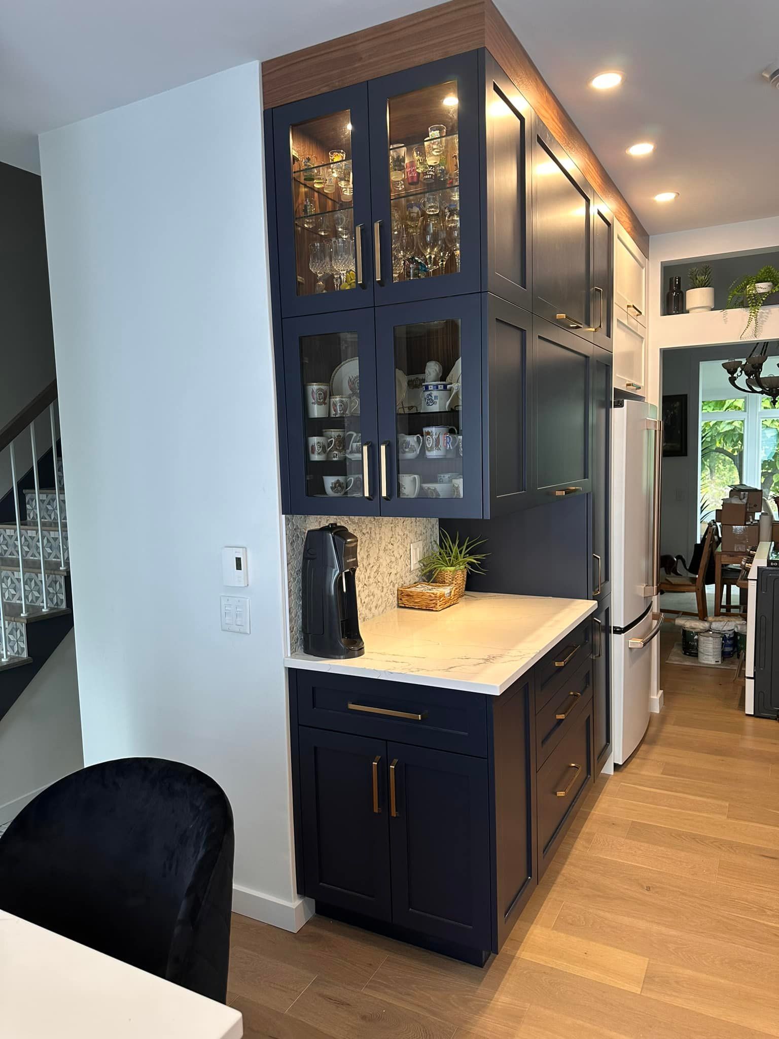 Cuisine équipée d'éléments bleu marine, comprenant une cafetière, une vitrine et un plan de travail.