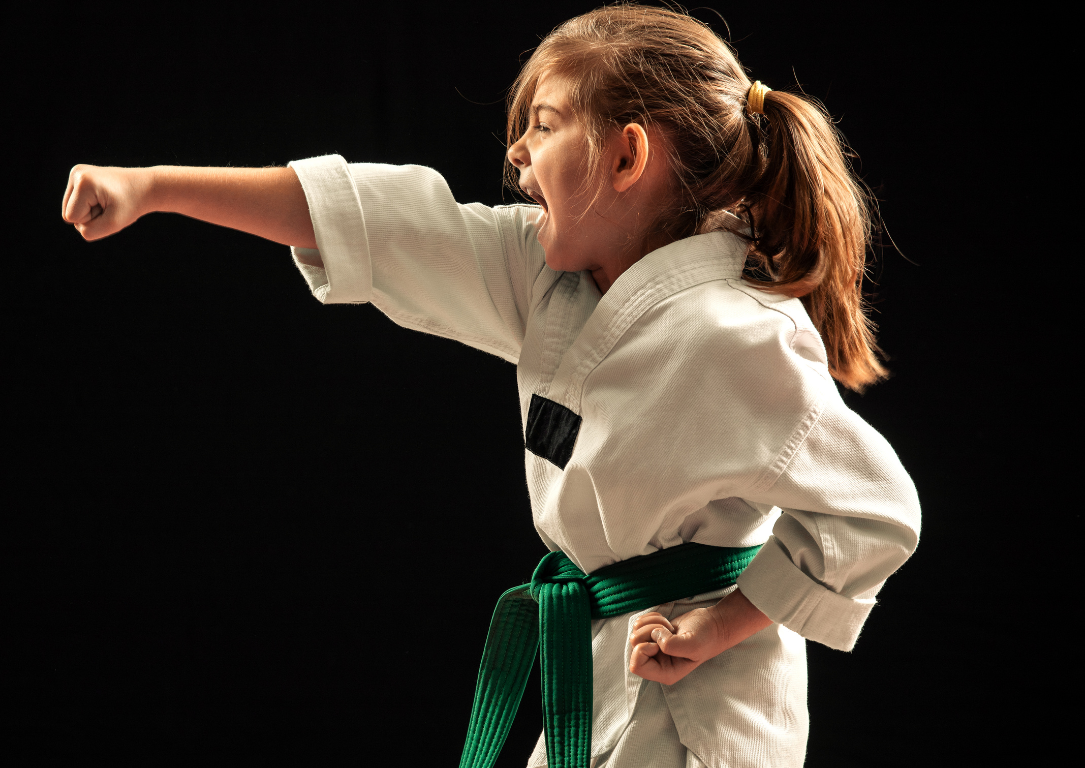 A young girl is wearing a white karate uniform and a green belt.