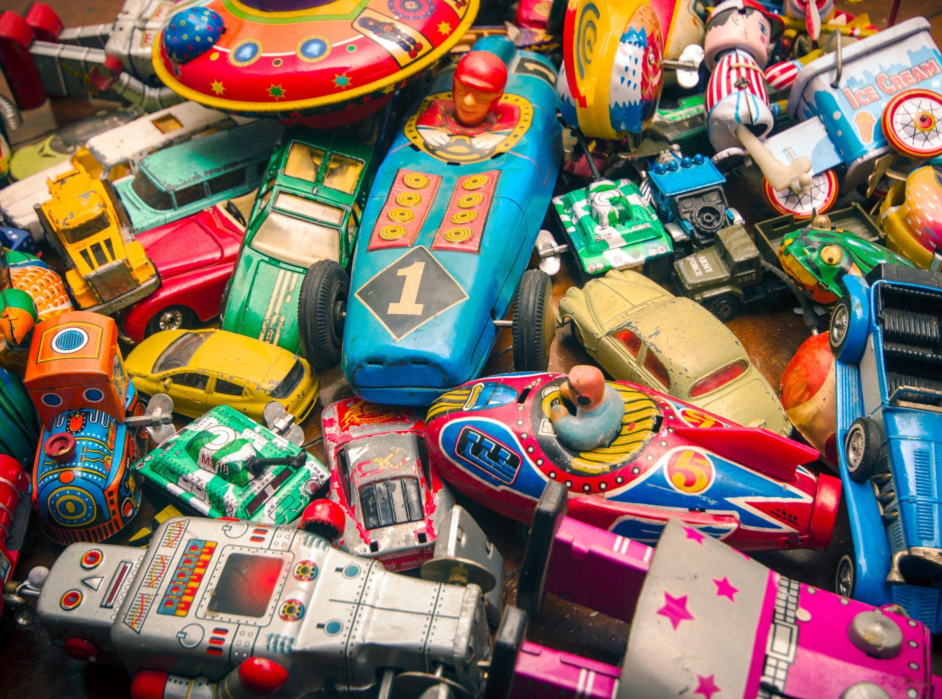 A wooden shelf filled with vintage 1980s toys, action figures, comics, and collectibles, including a Ghostbusters van.