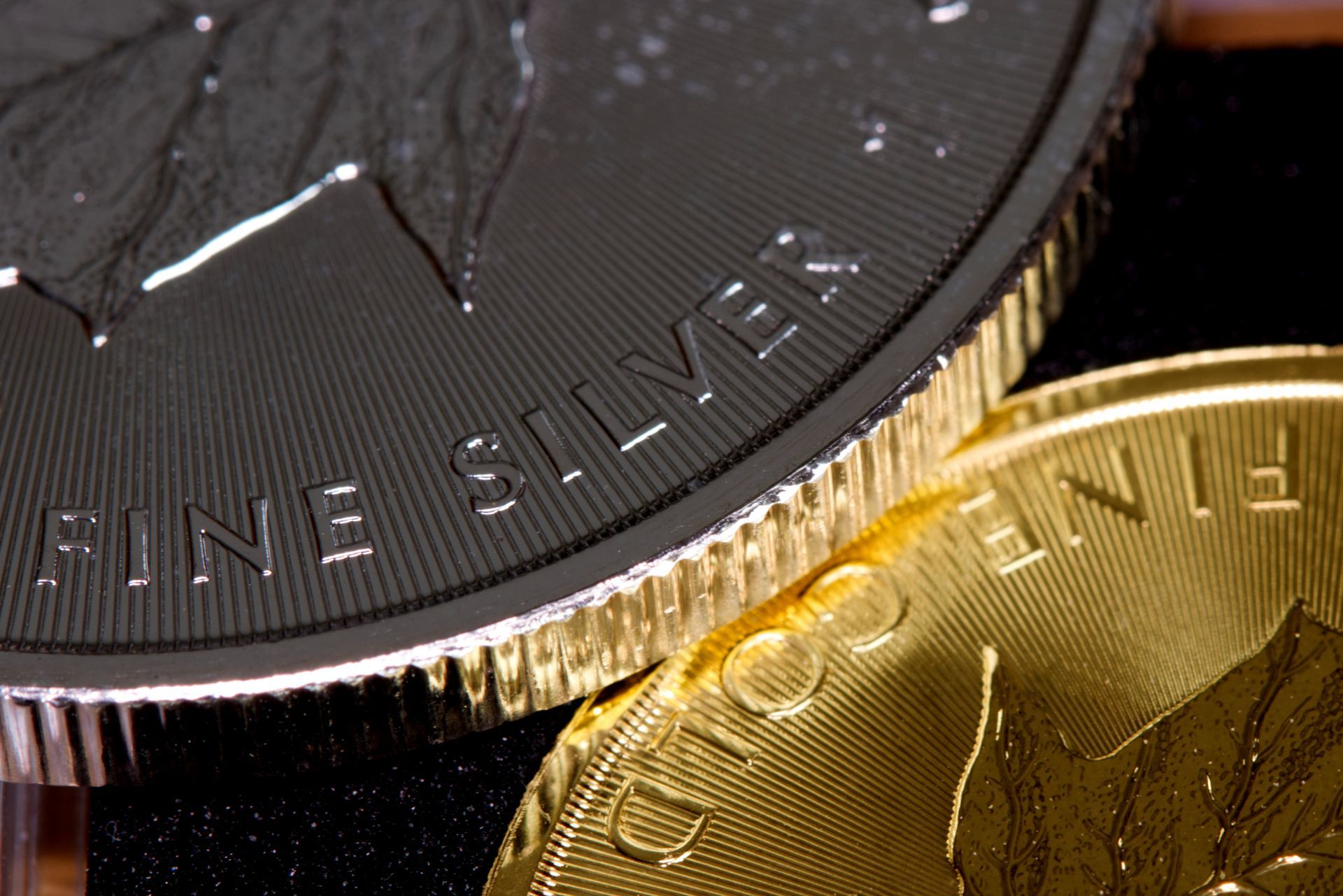 A top-down view of numerous varied metal coins overlapping one another, illuminated by high-contrast side lighting.