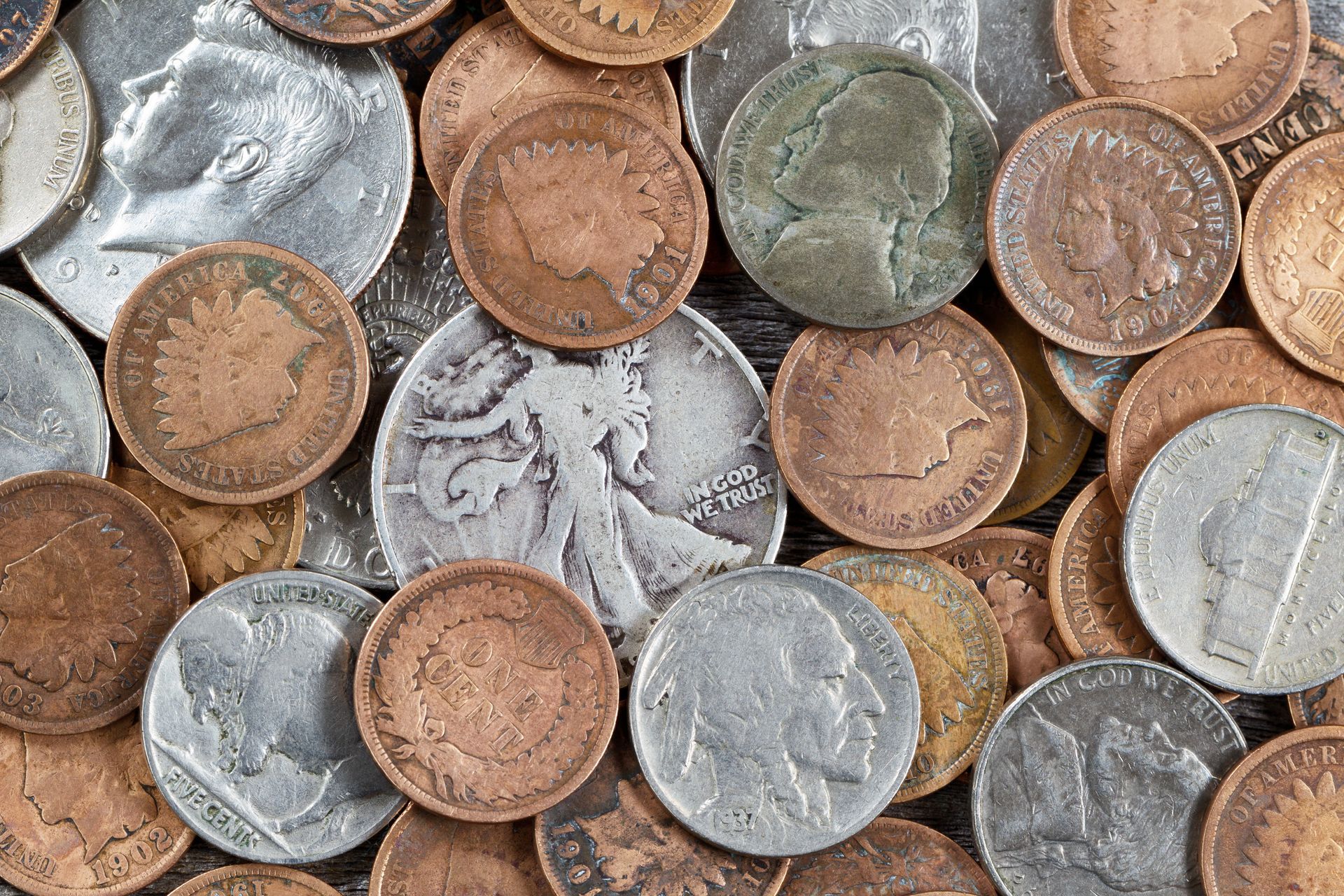 A top-down view of numerous varied metal coins overlapping one another, illuminated by high-contrast side lighting.