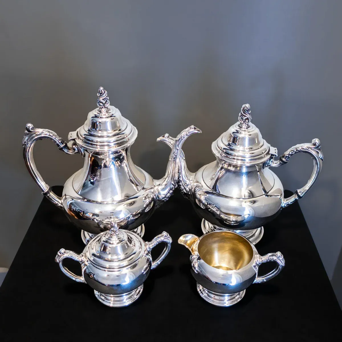 An ornate silver ewer and matching scalloped basin displayed in a dark setting, with a cloth resting in the foreground.