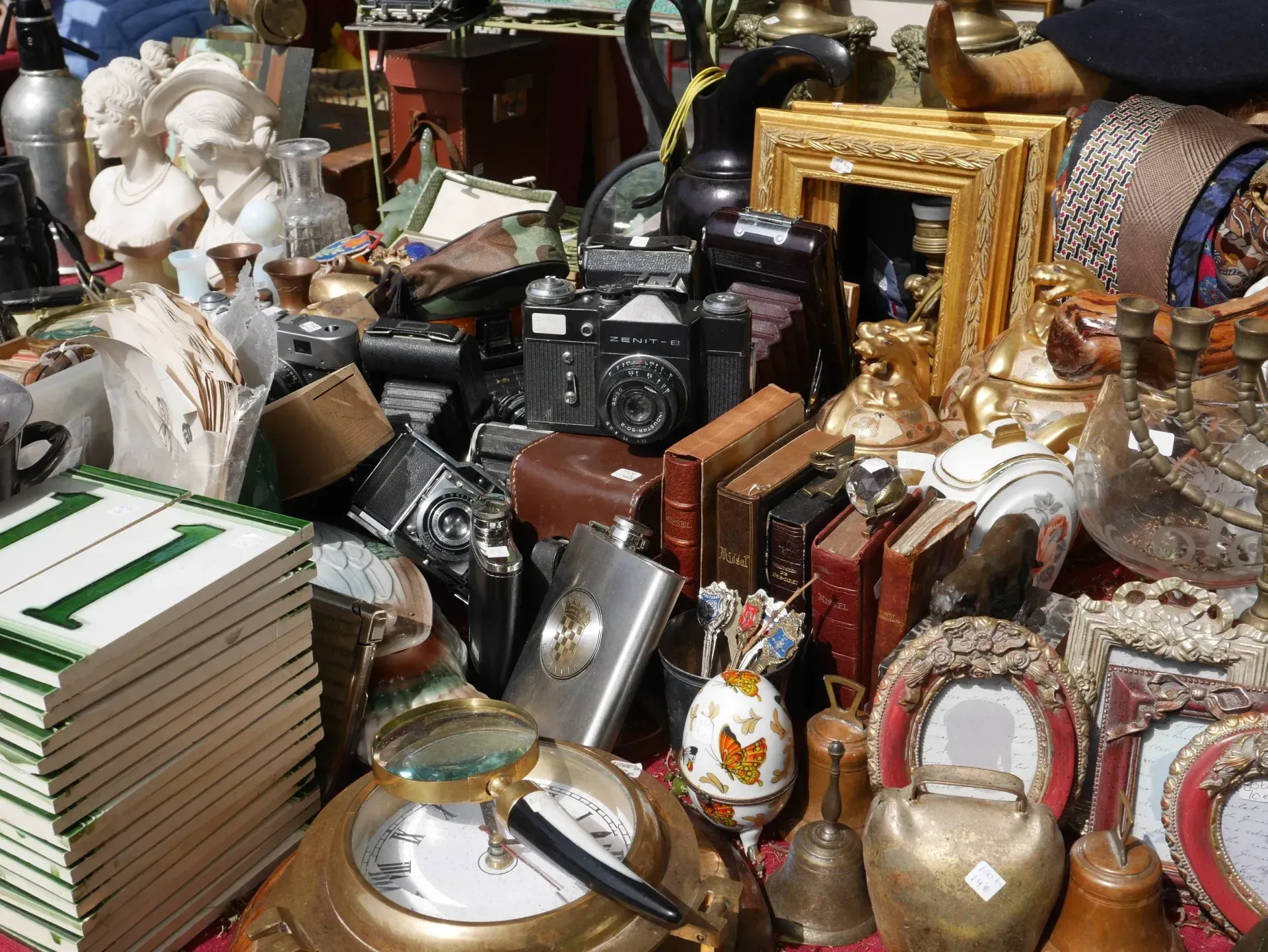 A cluttered collection of antiques, including vintage cameras, framed photos, books, a magnifying glass, and small statues.
