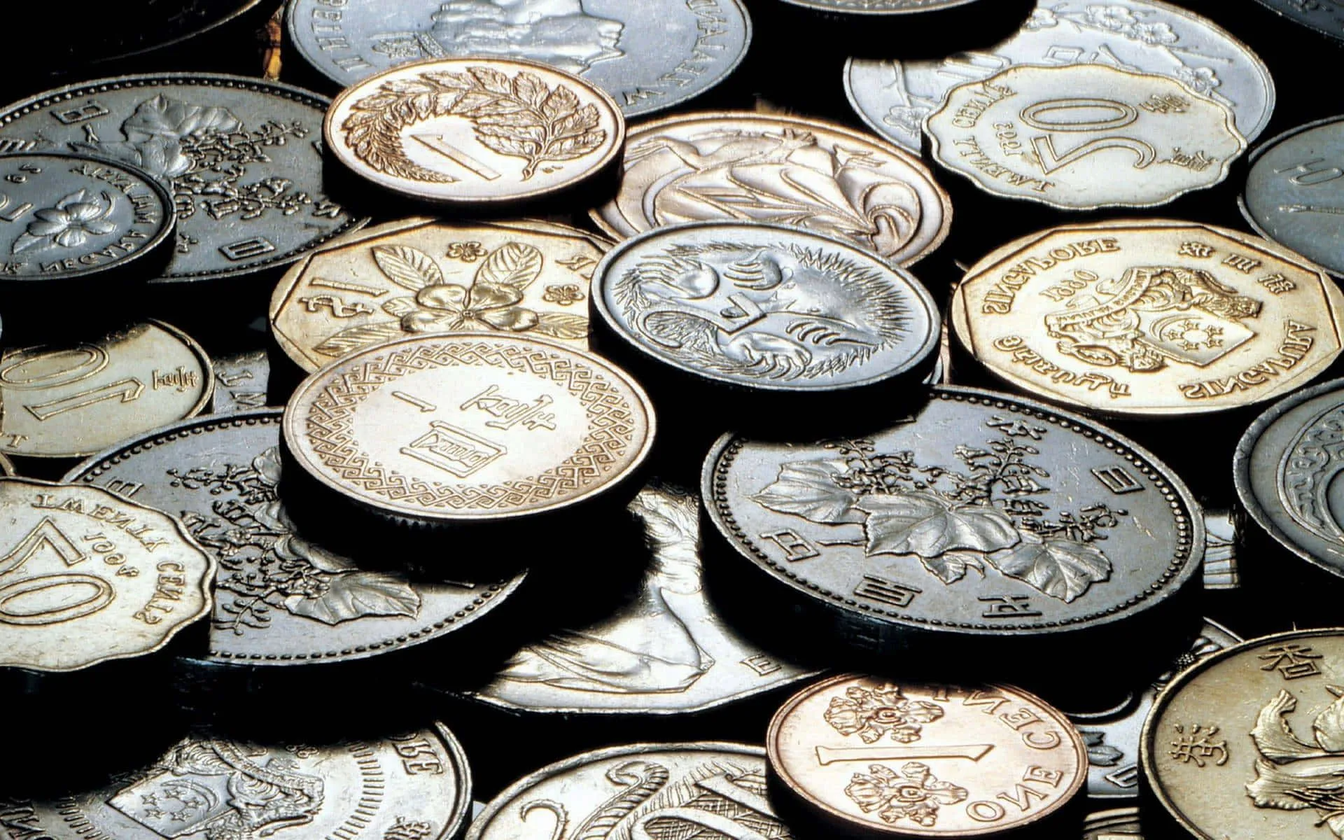 A collection of various vintage and modern silver, gold, and bronze coins scattered closely together in low light.