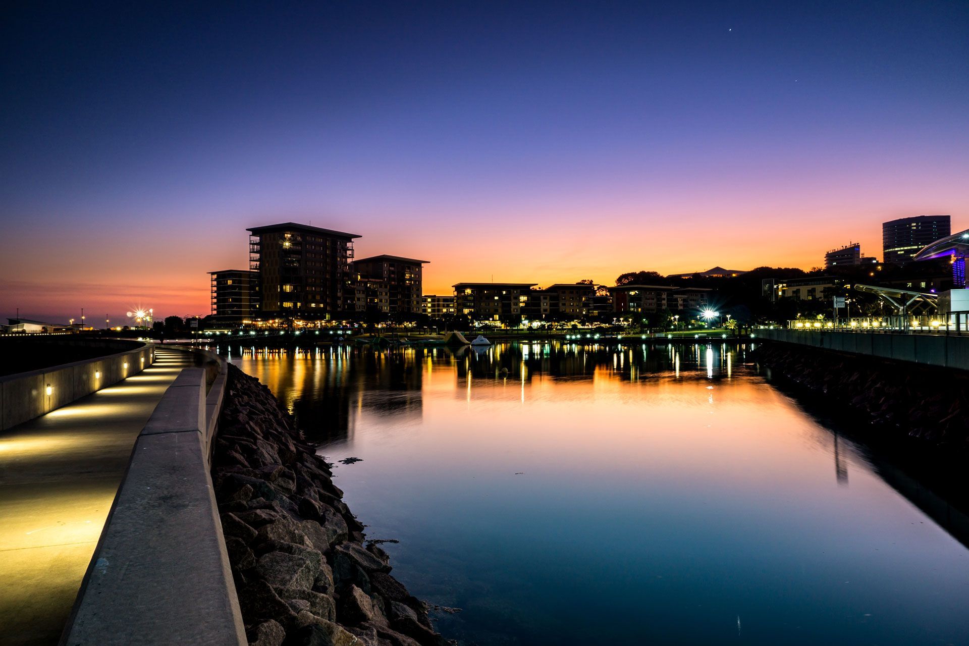 Evening cityscape reflecting in calm water; path with lights along the water's edge; purple and orange sunset — Industrial Automation Australia in Eagle Farm, QLD