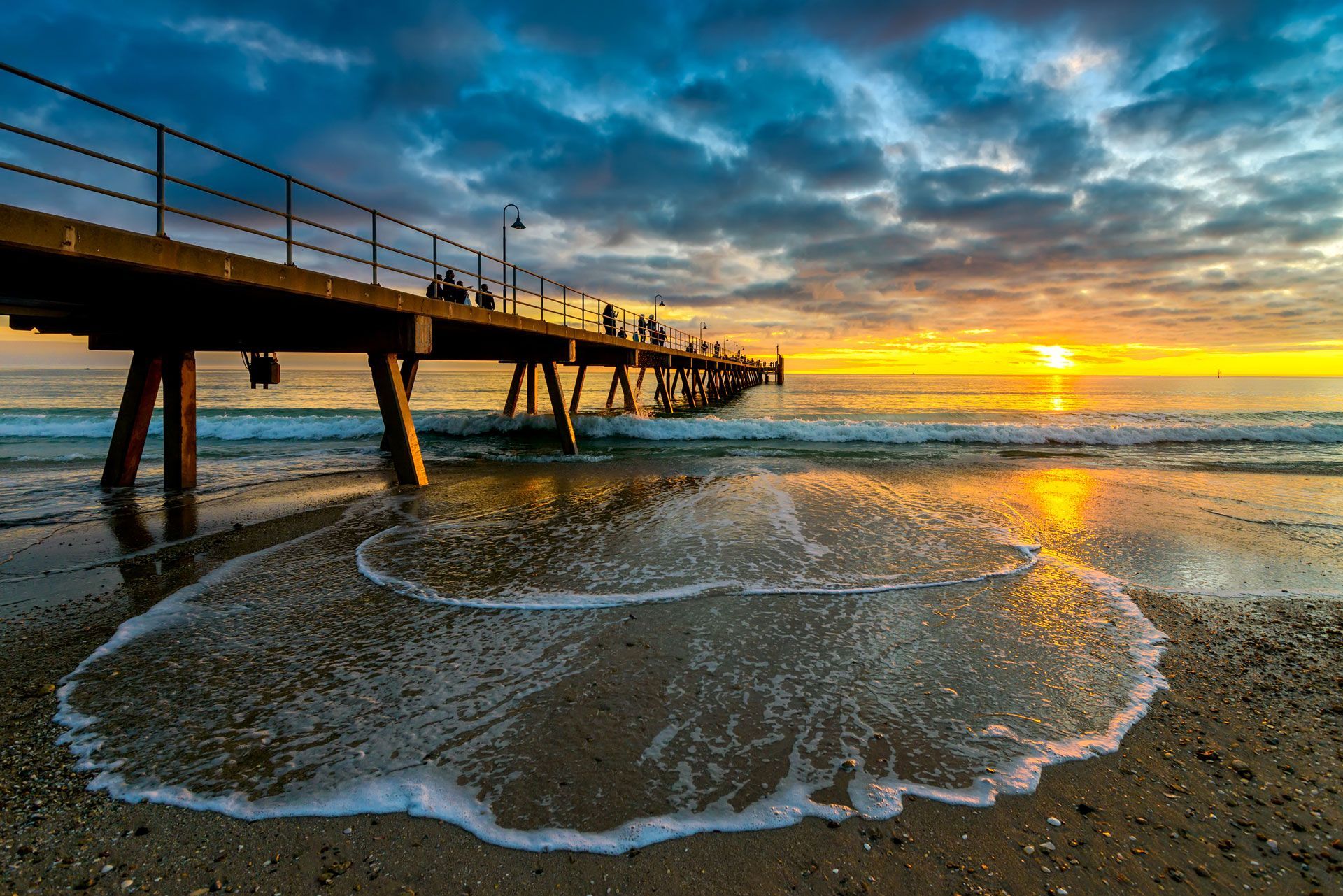 Sunset over ocean with pier; people walk along pier, sun reflects on wet sand — Industrial Automation Australia in Eagle Farm, QLD