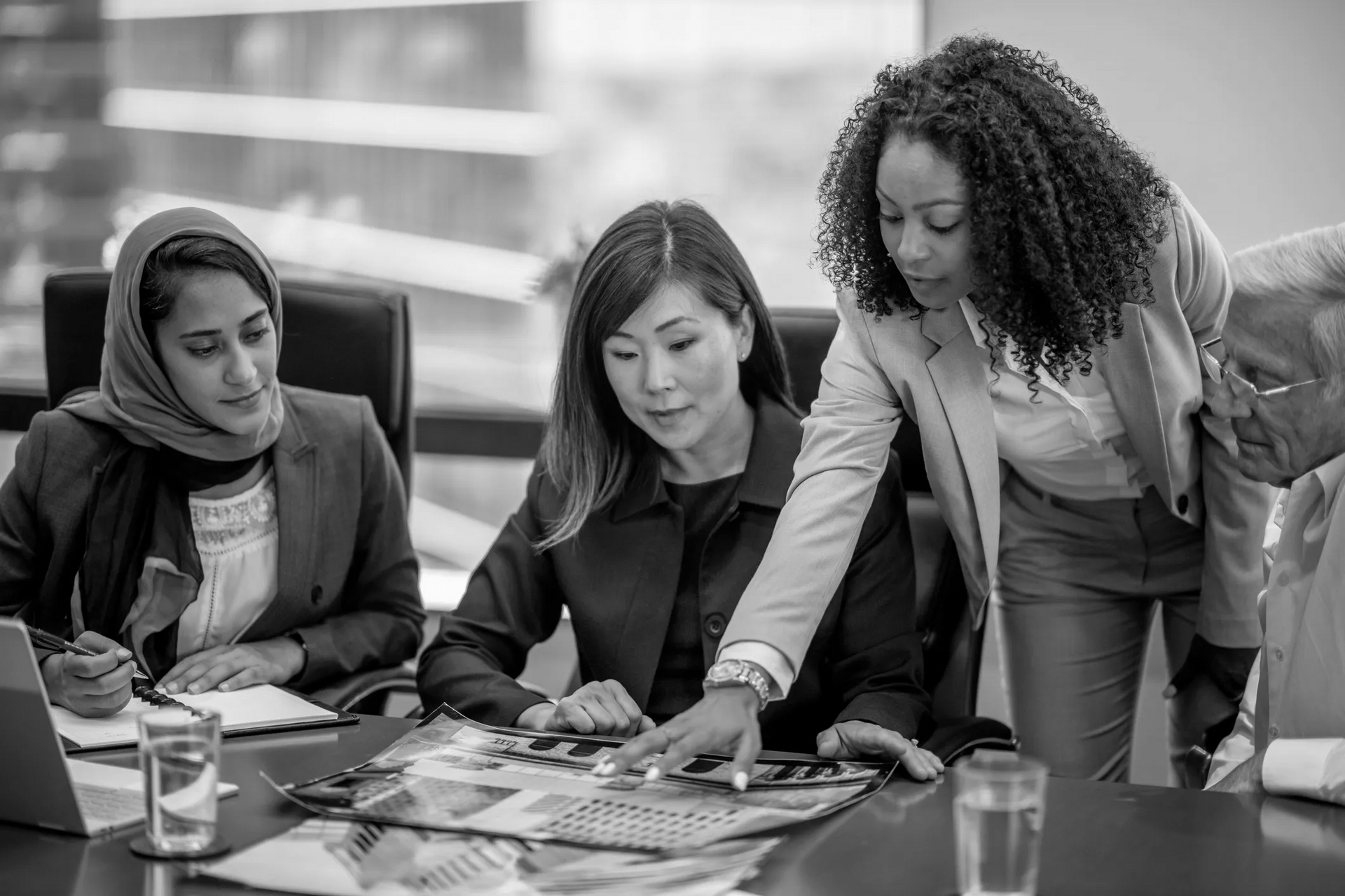Businesswomen reviewing documents at a conference table, discussing a project.