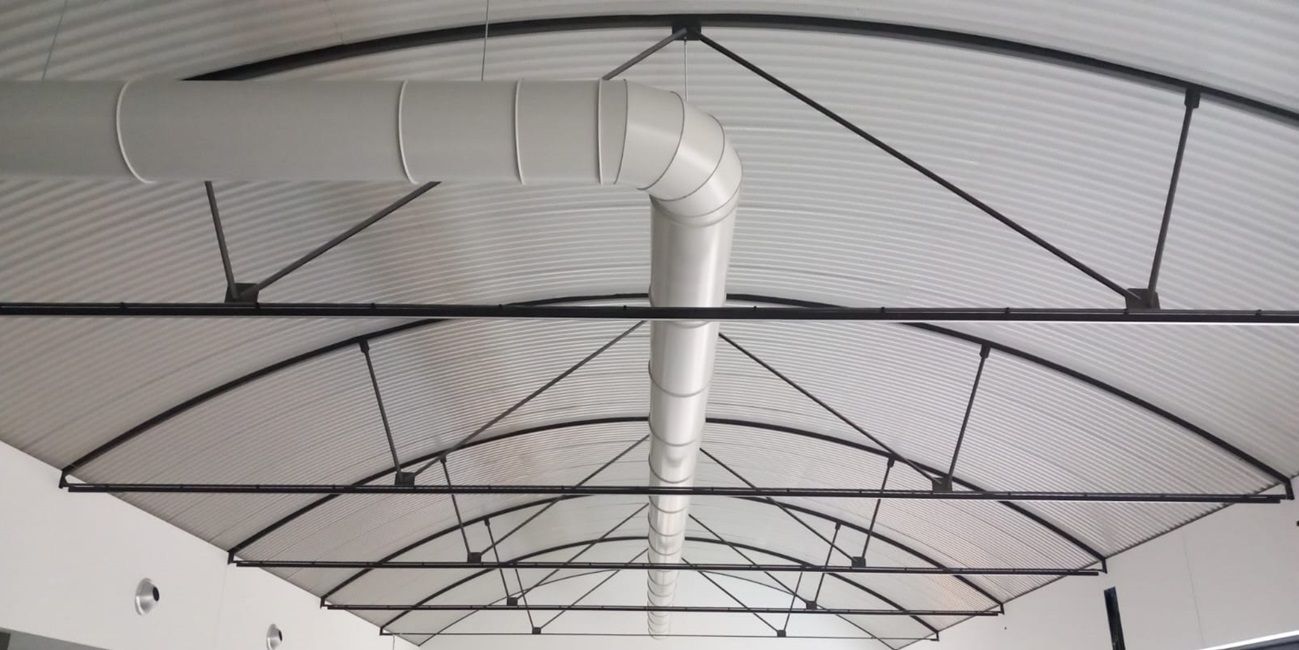 Gewelfd plafond van gegalvaniseerd metaal met zwarte steunbalken en geperforeerd ventilatiekanaal.