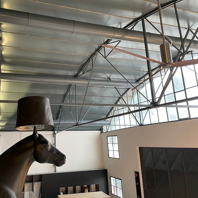 Een sculptuur van een paard met een lampenkap op zijn hoofd, in een modern, industrieel interieur met geperforeerde metalen luchtverdeelkanalen