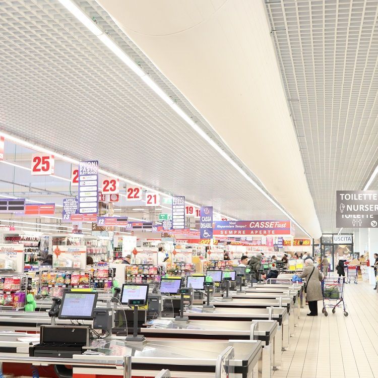 Kassa's in een supermarkt. Klanten en caissières bij de kassa. Wit plafond, fel licht, diverse producten en airsocks & luchtverdeelkanalen